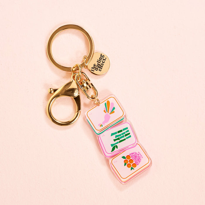 The Darling Effect’s Mahjong Tiles Acrylic Keychain features a lobster clasp, three colorful charms (bird, green bamboo, pink flower), and a round “unsung talents” tag—a stylish accessory for your bag or keys.