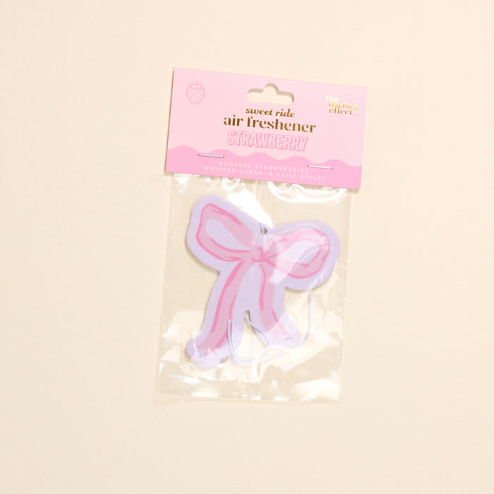 The-darling-effect's Bow Pink Sweet Ride Car Air Freshener features a strawberry scent, pink and purple bow shape, and plastic packaging for a unique, long-lasting aroma in your car.