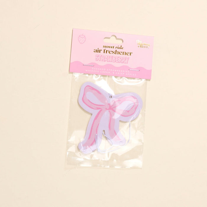 The-darling-effect's Bow Pink Sweet Ride Car Air Freshener features a strawberry scent, pink and purple bow shape, and plastic packaging for a unique, long-lasting aroma in your car.