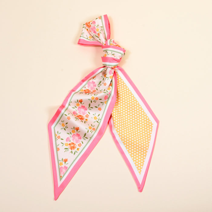 The Darling Effect's Endless Daydream Cream Twirl & Tie Scarf Accessory is a versatile silk scarf with pink edges, floral print on one end, and yellow polka dots on the other, all set against a light beige background.