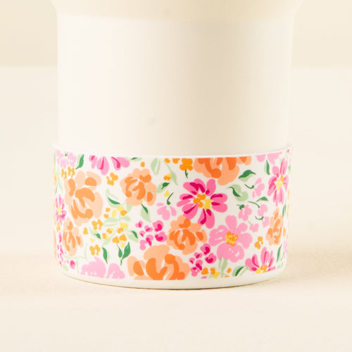 A white cup with a band of pink, orange, and yellow floral patterns around the bottom.
