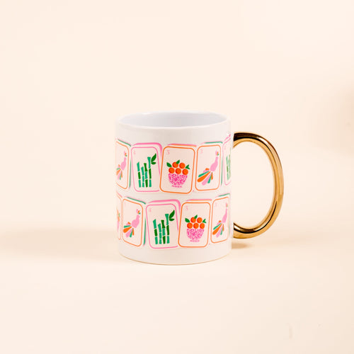The Darling Effect's Mahjong Tiles 11 oz Cozy Cute Ceramic Mug features a golden handle and vibrant playing card-style fruit, veggie, bamboo, and bird designs—perfect for coffee or tea on a plain light background.