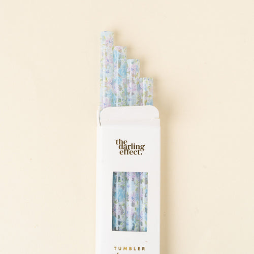 A white box labeled the-darling-effect. Secret Garden Blue 40 oz Tumbler Straw Set holds five BPA-free reusable straws with pastel floral patterns, arranged in a staggered row on a cream-colored background.