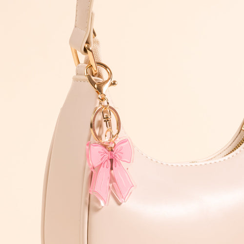 The Bow Pink Acrylic Keychain by the-darling-effect adds a cute touch to any cream-colored handbag with gold hardware, creating a warm, elegant vibe and making your bag a truly stylish accessory.