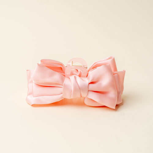 A large pink satin hair bow with a claw clip, displayed against a plain off-white background.