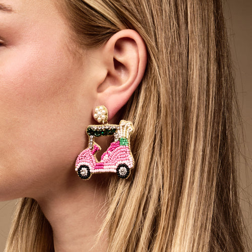A close-up of a woman with straight blonde hair wearing The Darling Effect’s Golf Cart Beaded Earrings, featuring a large pink golf cart with golf clubs—perfect for those who love bold, colorful accessories.