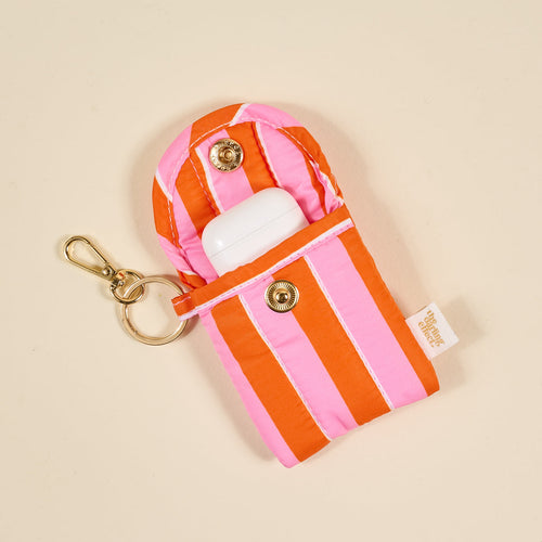 The Darling Effect Sicily Stripes Pink Puffy Earbud Case features pink and orange stripes, a gold keyring, and snap button. Open, it reveals a white wireless earbuds case inside.