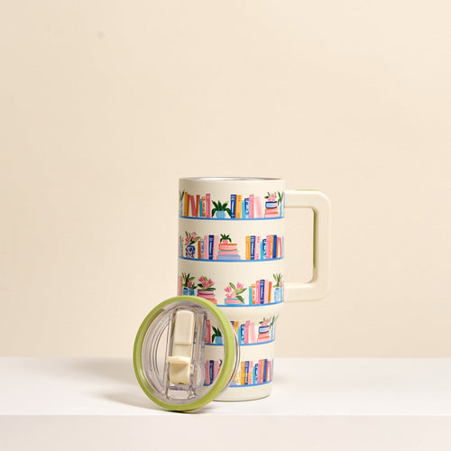 The Darling Effect Book Shelfie 20 oz Lifestyle Flip Straw Tumbler features a cream finish with a bookshelf design of colorful books and plants. 