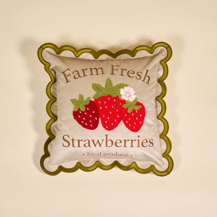 Square pillow with green scalloped edges, featuring an illustration of three strawberries and the text Farm Fresh Strawberries - local produce on a beige background.