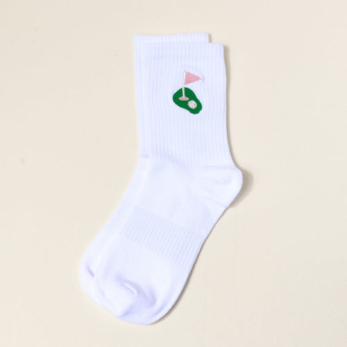 The Darling Effect Golf Embroidered Crew Socks: a white women's sock with a green putting green and pink flag design near the cuff, shown flat on a light beige background—ideal for fans of colorful, embroidered socks.