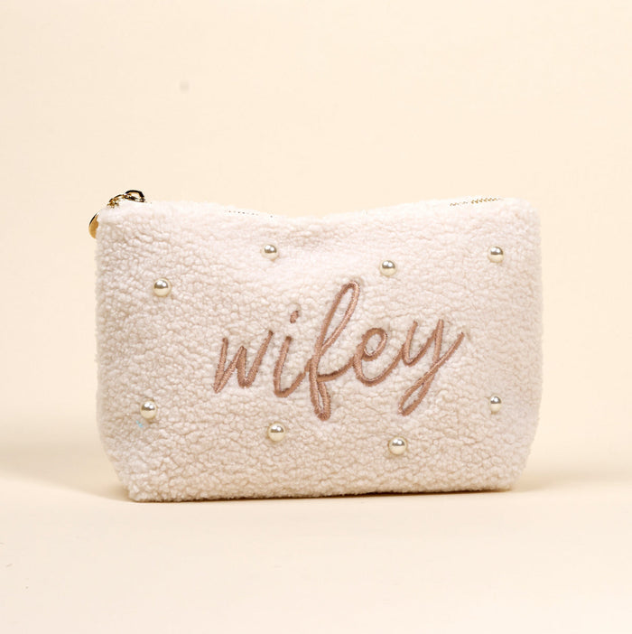 The Darling Effect Wifey & Pearls Teddy Pouch is a cream sherpa accessory, featuring embroidered "wifey" in script and scattered pearls—an adorable essential for any set.