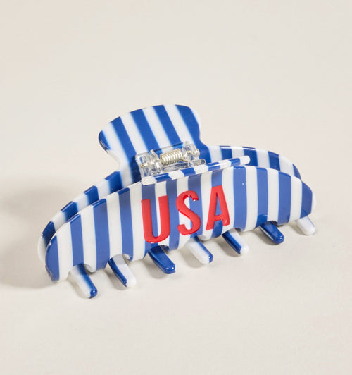A striped blue and white hair claw clip with the letters USA in red printed on the side, photographed on a light background.