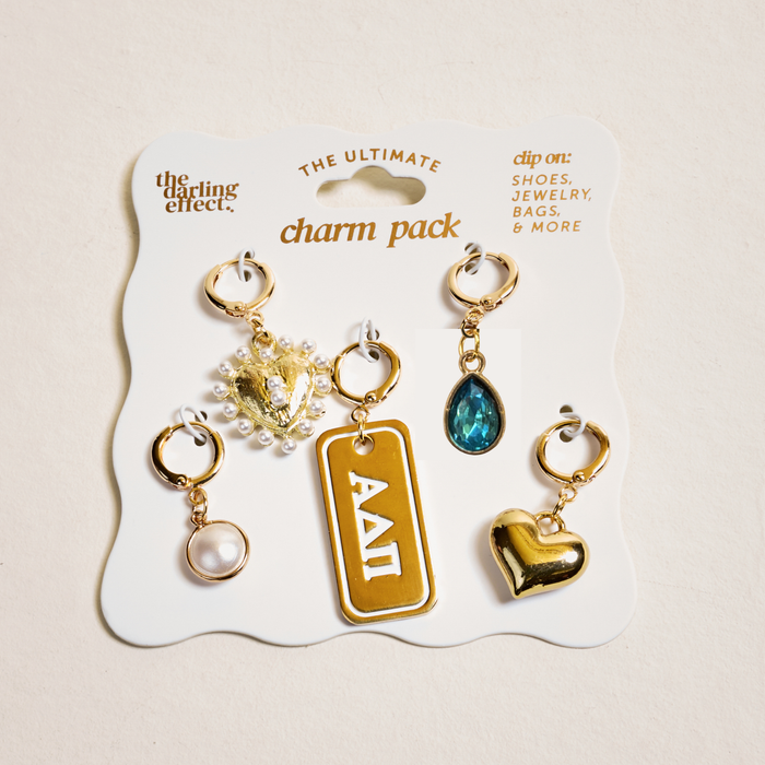 The Darling Effect’s Alpha Delta Pi The Ultimate Charm Pack includes five gold charms—a pearl, heart, blue teardrop gem, pearl and gold crest, and rectangular Greek letter—on a card labeled The Ultimate Charm Pack.