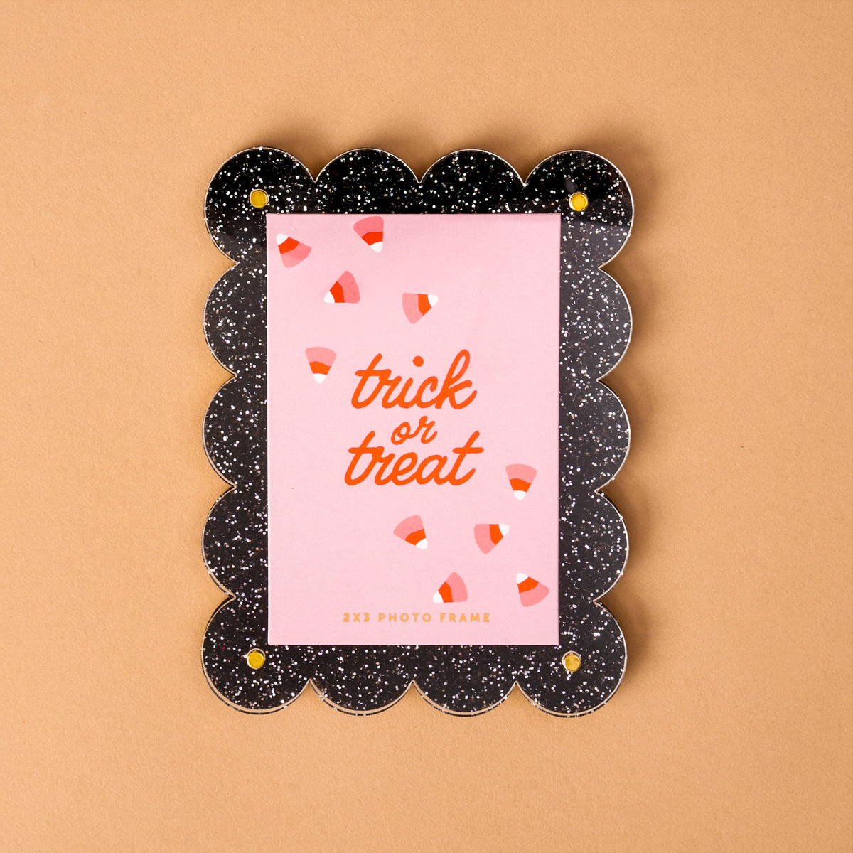 The Trick or Treat Mini Acrylic Picture Frame Magnet by The Darling Effect features a scalloped black design with white speckles and holds a pink card that says “trick or treat” in cheerful orange lettering, surrounded by candy corn illustrations. Set against a light brown background, this festive accessory is perfect for enhancing your magnetic photo display or creative mini photo frames collection.
