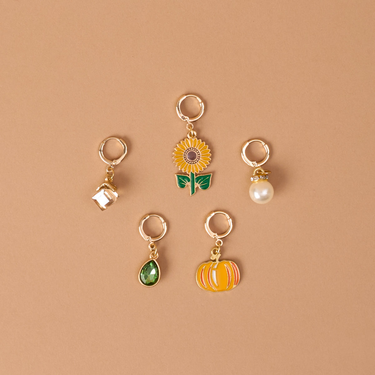 Sunflower Fields The Ultimate Charm Pack by The Darling Effect features five gold keychains—a white house, a sunflower, a pearl, a green teardrop gem, and an orange pumpkin—beautifully arranged on a tan background in a loose circular pattern.
