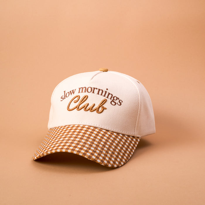 The Darling Effect’s Slow Mornings Club Classic Canvas Hat features “Slow Mornings Club” embroidered on the front and a brown-and-white checkered brim, all set against a beige background—a timeless accessory that’s perfect for everyday wear.