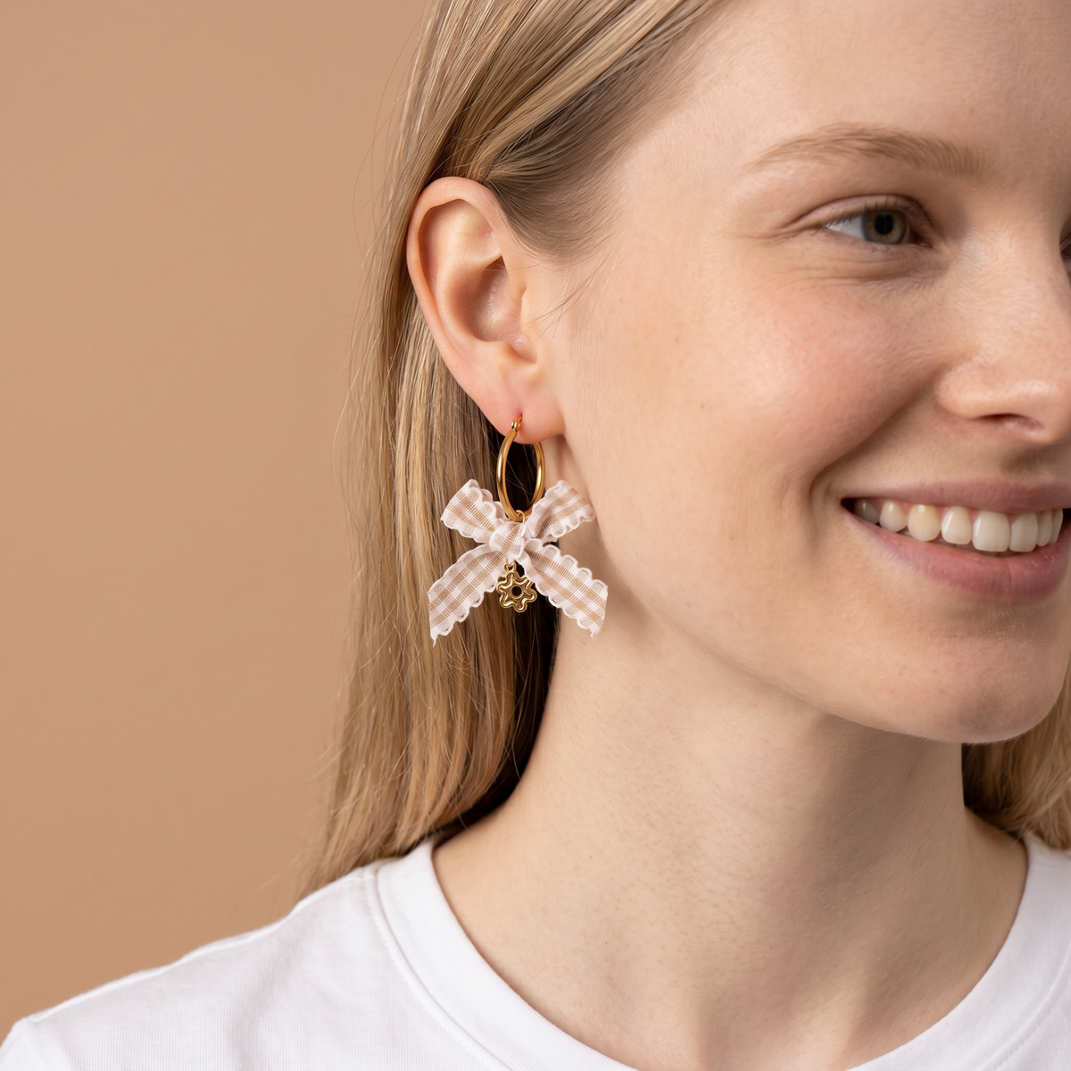 A woman with light skin and straight blonde hair wears a white top and The Darling Effect’s Harvest Honey Signature Hoop Earrings. She smiles softly against a plain beige background.