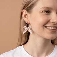 A woman with light skin and straight blonde hair wears a white top and The Darling Effect’s Harvest Honey Signature Hoop Earrings. She smiles softly against a plain beige background.