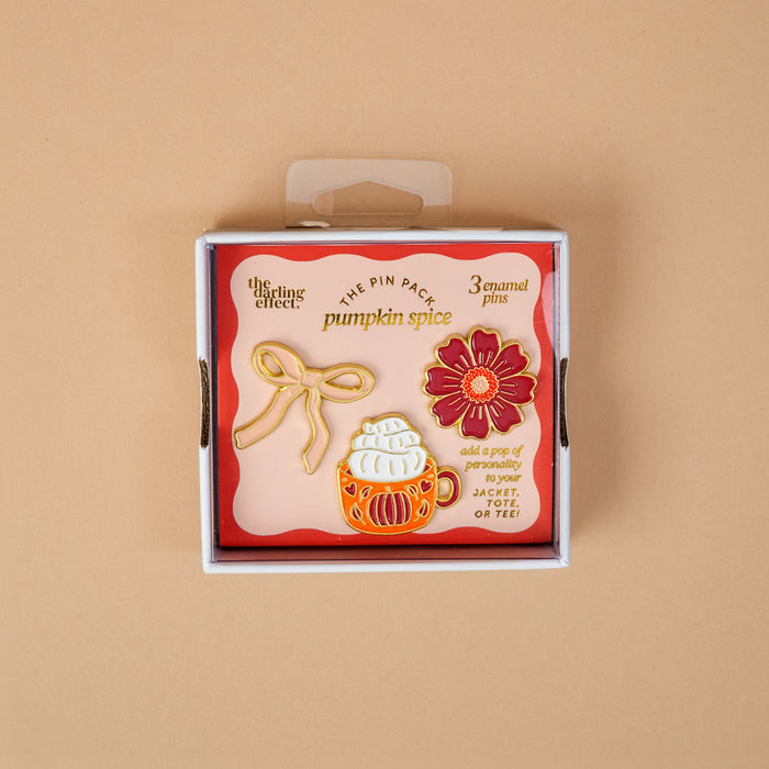 Introducing Pumpkin Spice The Pin Pack by The Darling Effect: a thoughtfully curated set displayed on a peach background, featuring three vibrant pins—a cheerful yellow bow, a cozy pumpkin spice latte, and a bright red flower. The packaging reads “pumpkin spice” and encourages you to add these collectible pins to your favorite jacket or tee.