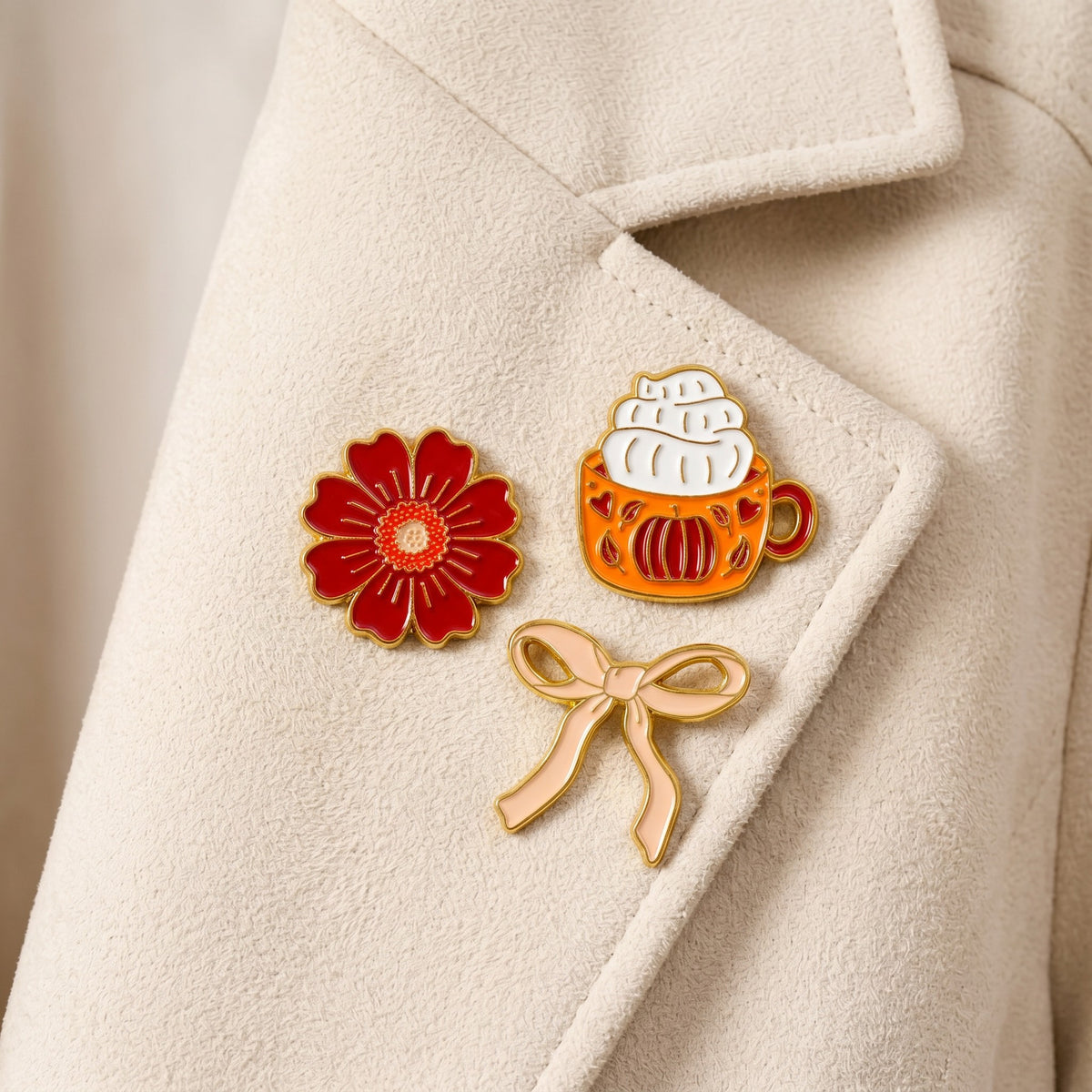 Pumpkin Spice The Pin Pack by The Darling Effect features three collectible pins—a red flower, an orange pumpkin mug topped with whipped cream, and a light gold ribbon bow—that add a touch of personality and charm to any outfit.