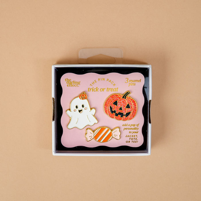 Introducing the Trick or Treat The Pin Pack by The Darling Effect: this charming set includes three enamel pins—a white ghost holding a pumpkin, an orange jack-o-lantern, and a striped candy. Designed as playful accessories for jackets or totes, each collectible pin comes packaged in a box that reads “trick or treat,” inviting you to showcase your festive style all season long.