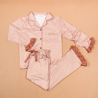 Experience cozy comfort and charming style with the Maple Gingham Sweet Dreams Pajama Pants Set from The Darling Effect. This pink and white checkered set features a long-sleeve button-up top paired with matching pants, both highlighted by playful ruffled cuffs for a feminine finish. The pants include a comfortable drawstring waist, making this set perfect for relaxing nights in or as an adorable gift option. Displayed on a beige background.