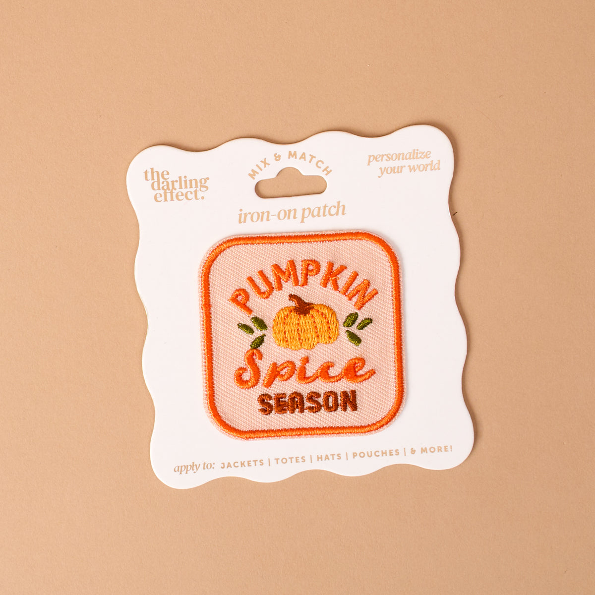 The Darling Effect’s On Patch-Pumpkin Spice Season Mix & Match Iron is a square iron-on patch featuring an orange pumpkin and the phrase “Pumpkin Spice Season” embroidered on it, displayed on beige packaging. Perfect for customizing clothing or accessories, this patch adds a cozy touch to any colorful collection.