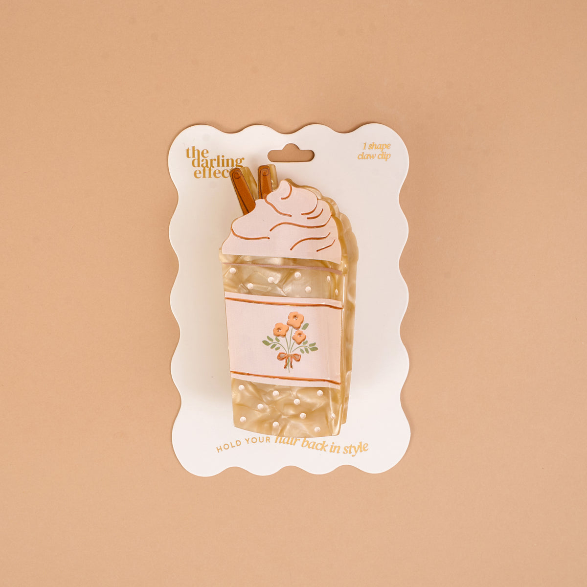Add a splash of whimsy to your look with The Darling Effect’s Coffee Run Shape Up Claw Clip, designed as a charming whipped cream-topped drink complete with brown straws and subtle floral details. Perfect for crafting cute hairstyles, this playful hair accessory comes displayed on a scalloped-edged backing card set against a beige background.