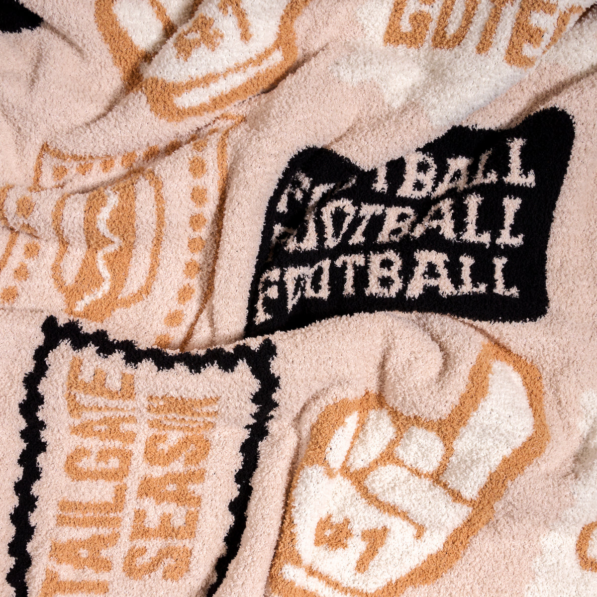 Introducing the Huddle Up Cozy Dreams Luxe Blanket by The Darling Effect—a beige and black ultra-soft polyester microfiber throw featuring football-themed graphics like a foam finger, bold FOOTBALL lettering, and stylized patches and text. Perfect for fans who want to stay cozy and show team spirit.