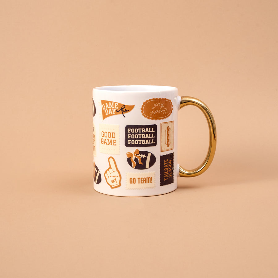 Enjoy your favorite drink on game day with The Darling Effect’s Huddle Up 11 oz Cozy Cute Ceramic Mug—a white ceramic mug featuring a gold handle, elegant gold accents, and football-themed stickers with phrases like “Game Day,” “Good Game,” “Go Team!” and “Football Football Football,” all set against a stylish beige background.