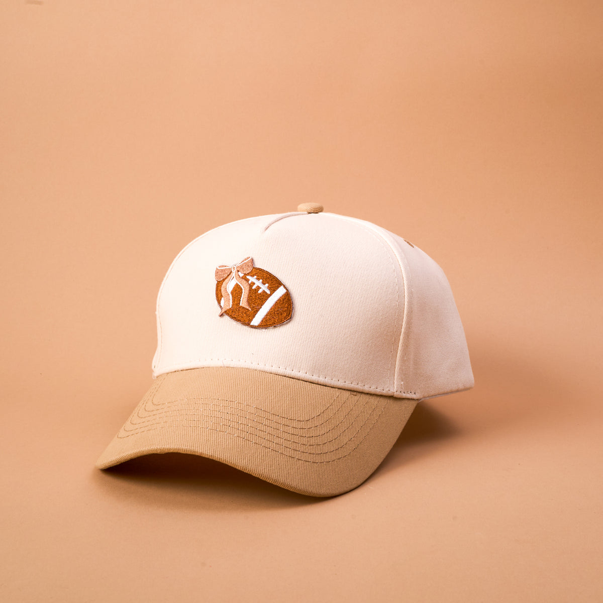 Introducing the Fab Football Classic Canvas Hat by The Darling Effect—a tan and beige casual hat featuring a brown football with white stitching design on the front. This relaxed fit accessory is shown against a plain beige background.