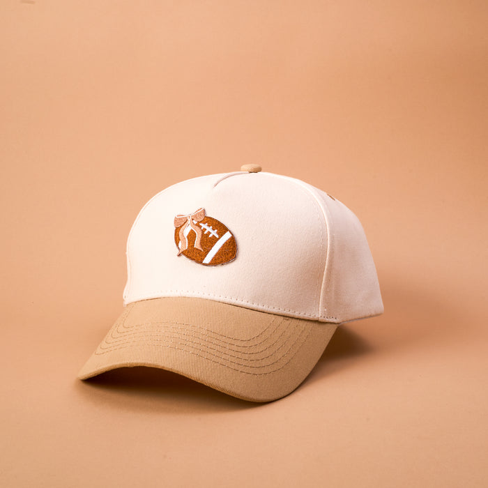 Introducing the Fab Football Classic Canvas Hat by The Darling Effect—a tan and beige casual hat featuring a brown football with white stitching design on the front. This relaxed fit accessory is shown against a plain beige background.