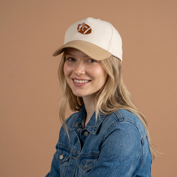 A smiling person with long blonde hair wears The Darling Effect’s Fab Football Classic Canvas Hat and a denim jacket, posing against a plain light brown background.