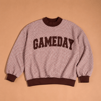 The Gameday Mockneck Sweatshirt by The Darling Effect features a brown and cream checkered design with “GAMEDAY” in bold brown letters across the front, shown against a solid tan background.