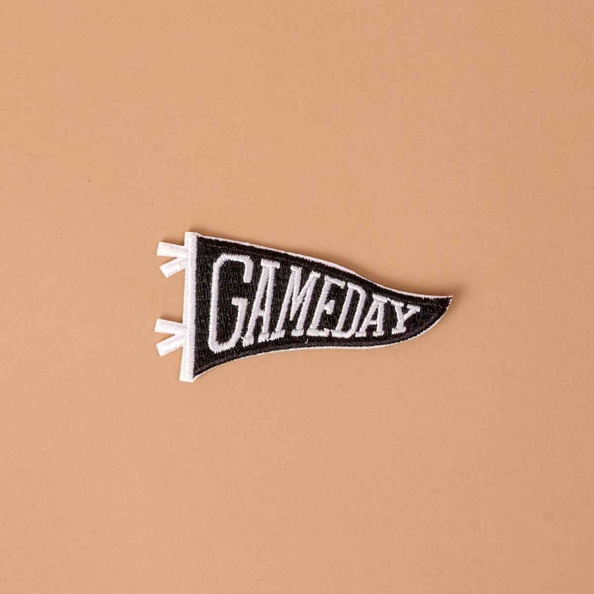 Introducing the Gameday Black Mix & Match Iron-On Patch by The Darling Effect—a black and white felt pennant patch featuring the word "GAMEDAY" in bold capital letters on a simple beige background, perfect for customizing your favorite items with a unique and stylish touch.