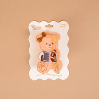 Add a sporty touch to your hairstyle with the Touchdown Teddy Shape Up Claw Clip by The Darling Effect—a teddy bear-shaped hair accessory featuring a brown bow, packaged on a white wavy-edged card with "The Darling Effect" and "Hold your hair back in style." The adorable bear illustration wears a letterman jacket and holds a football, making this claw clip perfect for cute, game-day looks.