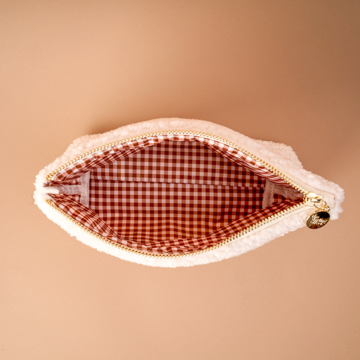 The Football & Pearls Teddy Pouch by The Darling Effect is a small white sherpa pouch featuring a gold zipper and a red and white gingham interior, displayed open against a beige background. It's the perfect addition to any accessory collection.