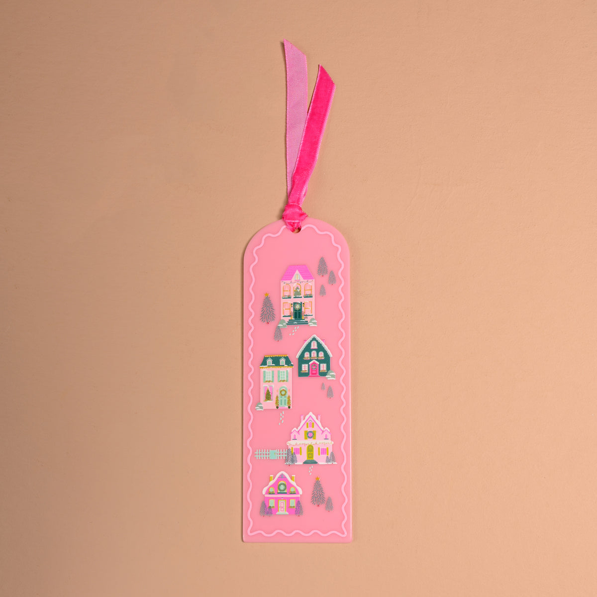 Pink Pine Village Acrylic Bookmark, a pink rectangular acrylic bookmark illustrated with four winter houses and pine trees, finished with a velvet ribbon tie at the top.