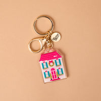 BowBelle Manor acrylic keychain featuring a pink and white house with green wreaths on the windows and a pink door, attached to a gold keyring.