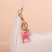 A Cranberry Cosmo Acrylic Keychain shaped like a pink cocktail with a red bow and green garnish, attached to a white shoulder bag as a stylish accessory.