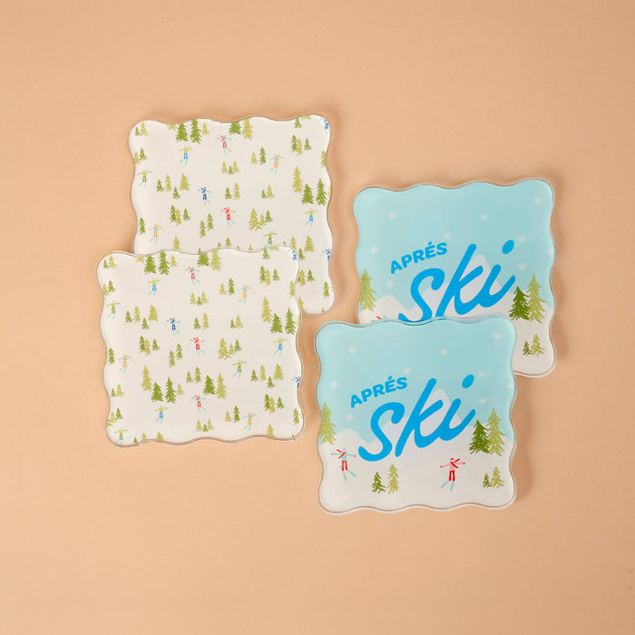 Aprés Ski Table Talk Acrylic Coaster Set featuring four scalloped square acrylic coasters: two decorated with skiers and evergreen trees, and two with Après ski text and seasonal designs.
