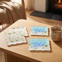 Four Aprés Ski Table Talk Acrylic Coaster Set coasters on a wooden table, including two with a forest print and two featuring the text Après ski with illustrated skiers.