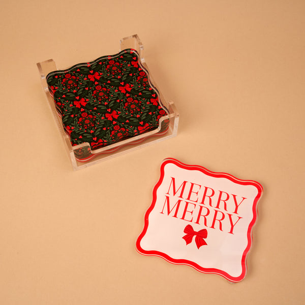 A Merry Moment Table Talk Acrylic Coaster Set featuring scalloped coasters in a clear holder, one printed with a red bow and MERRY MERRY alongside others with dark green holly and bows.