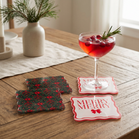 Four A Merry Moment Table Talk Acrylic Coaster Sets on a wooden table, two with a dark floral pattern and two with a red MERRY MERRY script and bow design, one holding a glass of red cocktail garnished with cranberries and a sprig of rosemary.