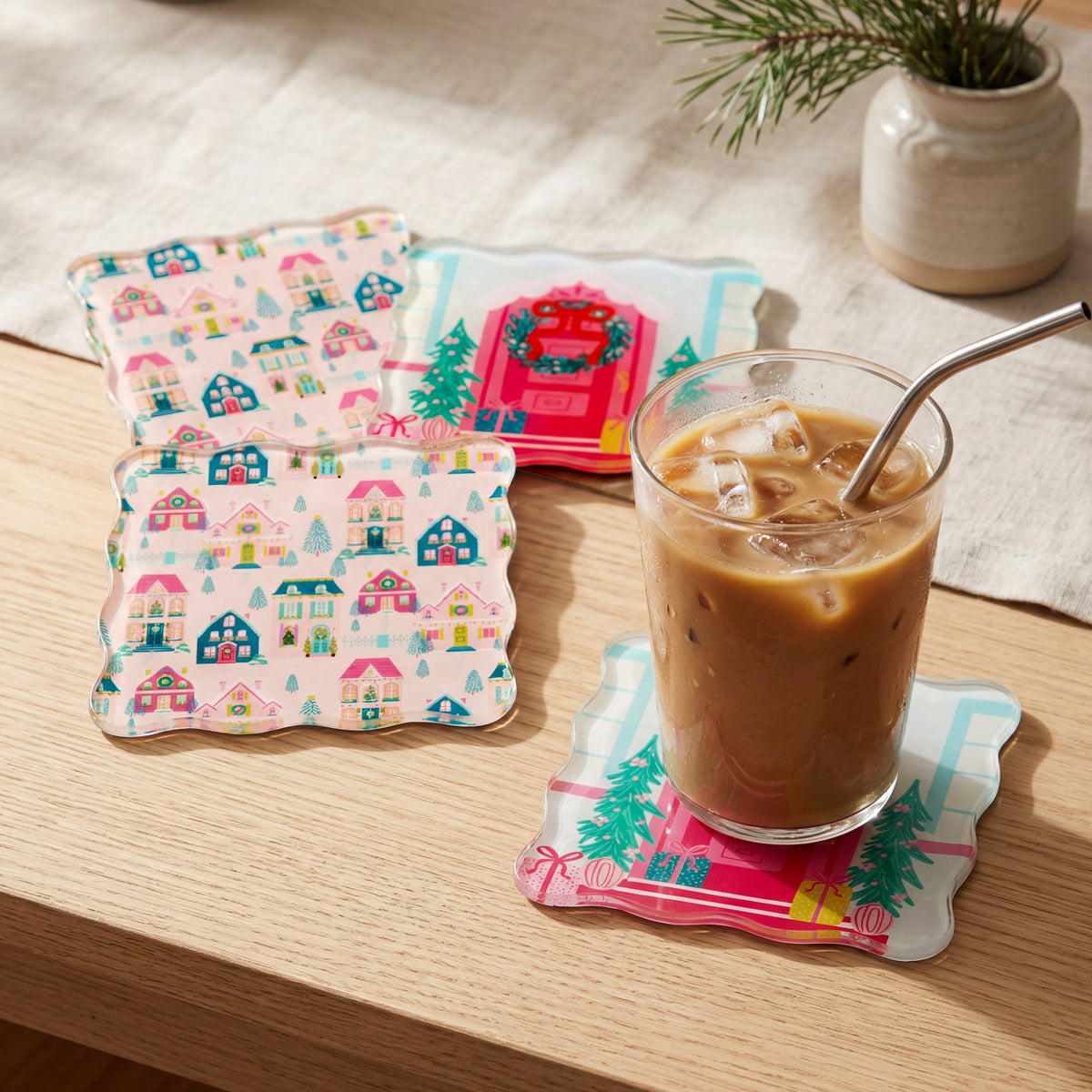 Sugarplum Lane Table Talk Acrylic Coaster Set featuring three square coasters with festive holiday house and entryway patterns, with a glass of iced coffee resting on one.