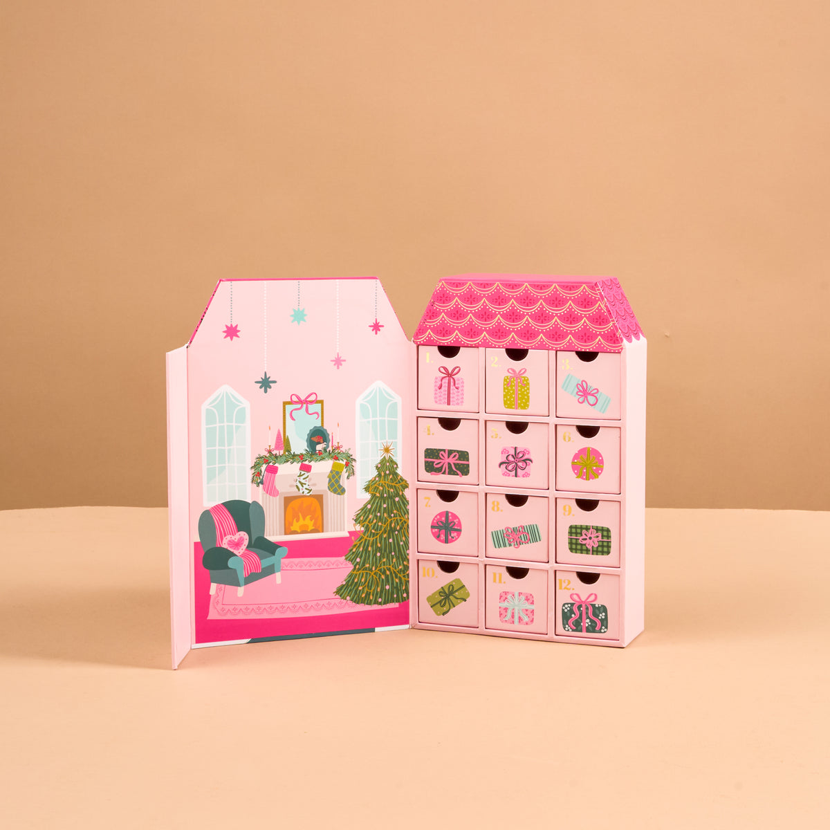 The Adoring Ornaments Ornament Advent Calendar is a house-shaped advent calendar with twelve numbered drawers and a decorative interior illustration of a cozy living room with a Christmas tree and fireplace, designed for miniature acrylic ornaments.