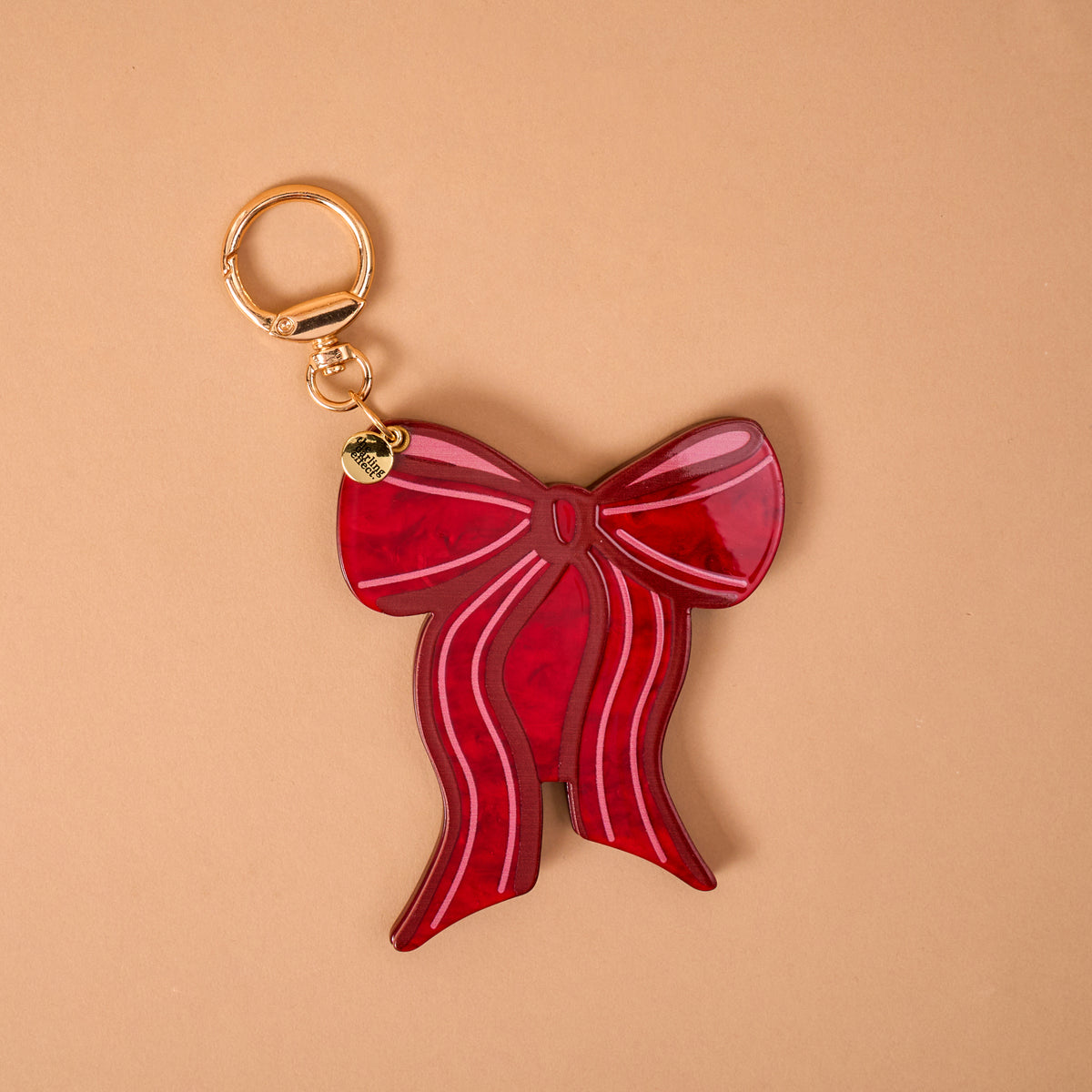 A Red Bow Mini Mirror Bag Charm by The Darling Effect, featuring a red, bow-shaped acrylic mirror, a gold-toned keyring, and a small branded circular tag.