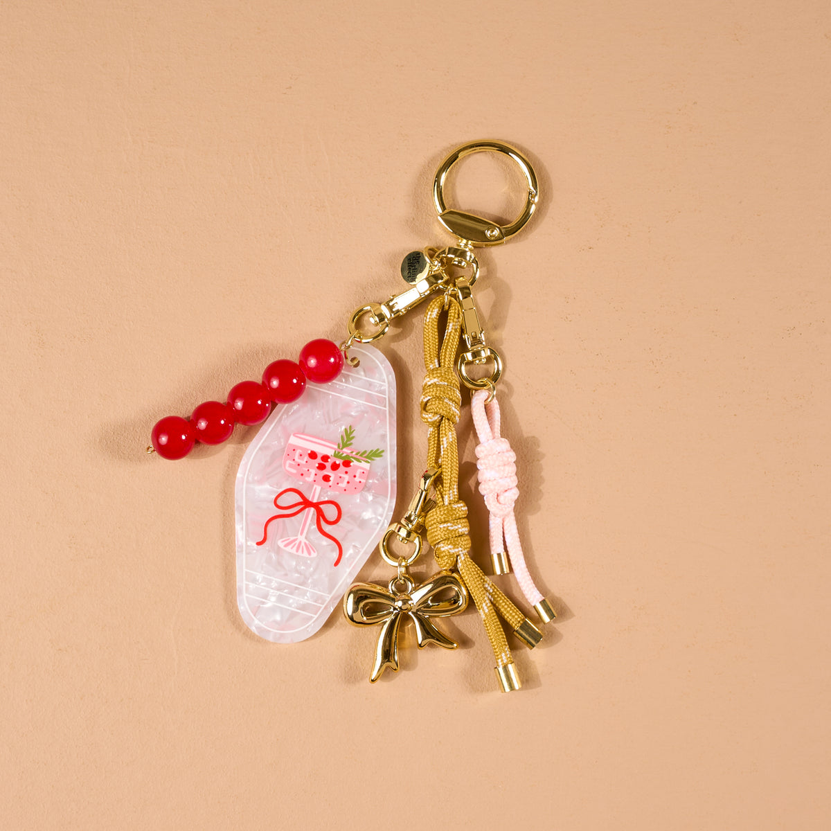 Cranberry Cosmo Motel Key Bag Charm featuring a red beaded strand, a pink cocktail glass charm, a gold bow, and knotted cord tassels, serving as a vintage accessory.