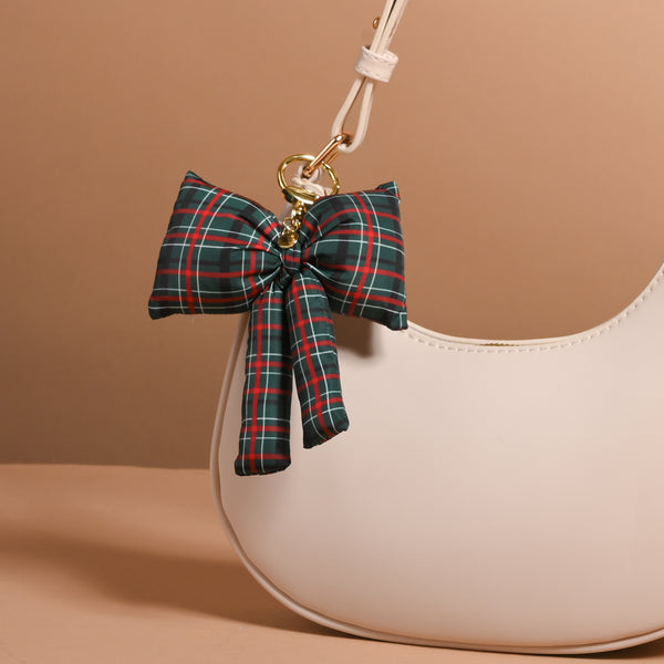 Classic Plaid Puffy Bow Bag Charm in a green, red, and black plaid pattern, attached to a cream-colored handbag with a gold-toned clip.