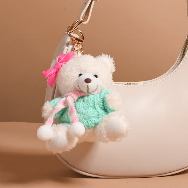 An Arctic Angel Teddy Bear Bag Charm wearing a green sweater, a pink and white striped scarf, and a pink hair bow, clipped to a cream-colored handbag.